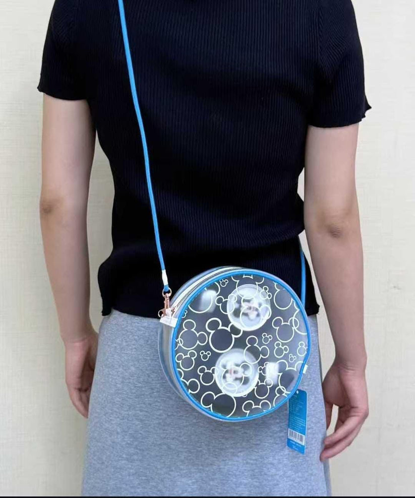 Person wearing a transparent round bag with blue strap on a plain background and showing Headphones carying safely