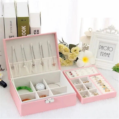 Pink jewelry box with compartments filled with jewelry on a white surface.