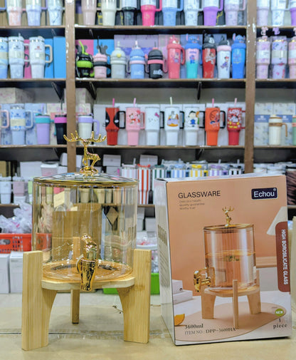 Glass Juice dispenser with gold accents on a stand next to an Echou product box in a store setting.