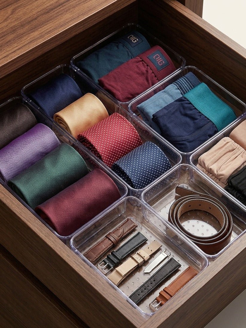 Organized drawer with compartments holding ties, belts, and other accessories.